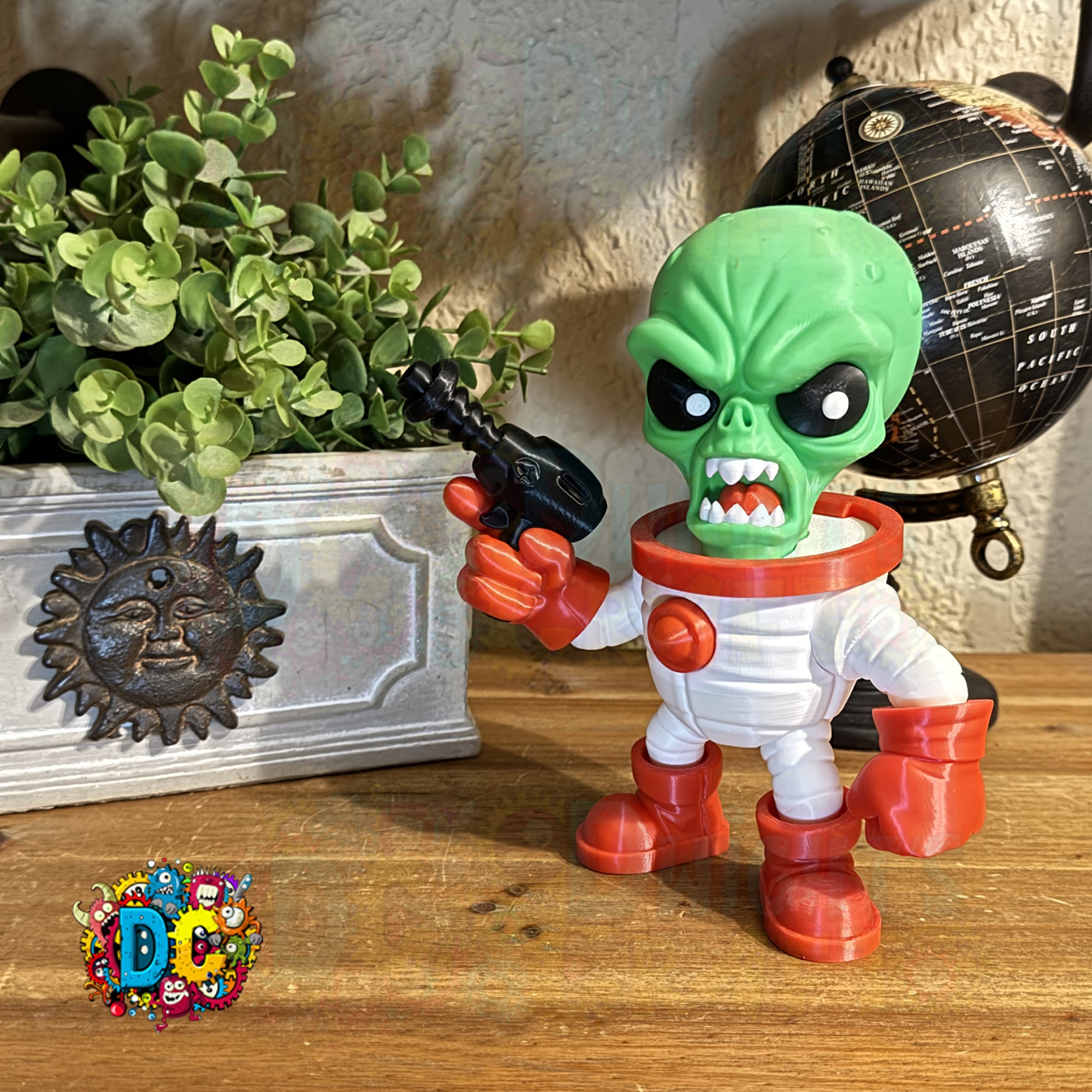 Toy figure of a green alien in a white suit with red boots on a wooden surface, next to a plant and globe.