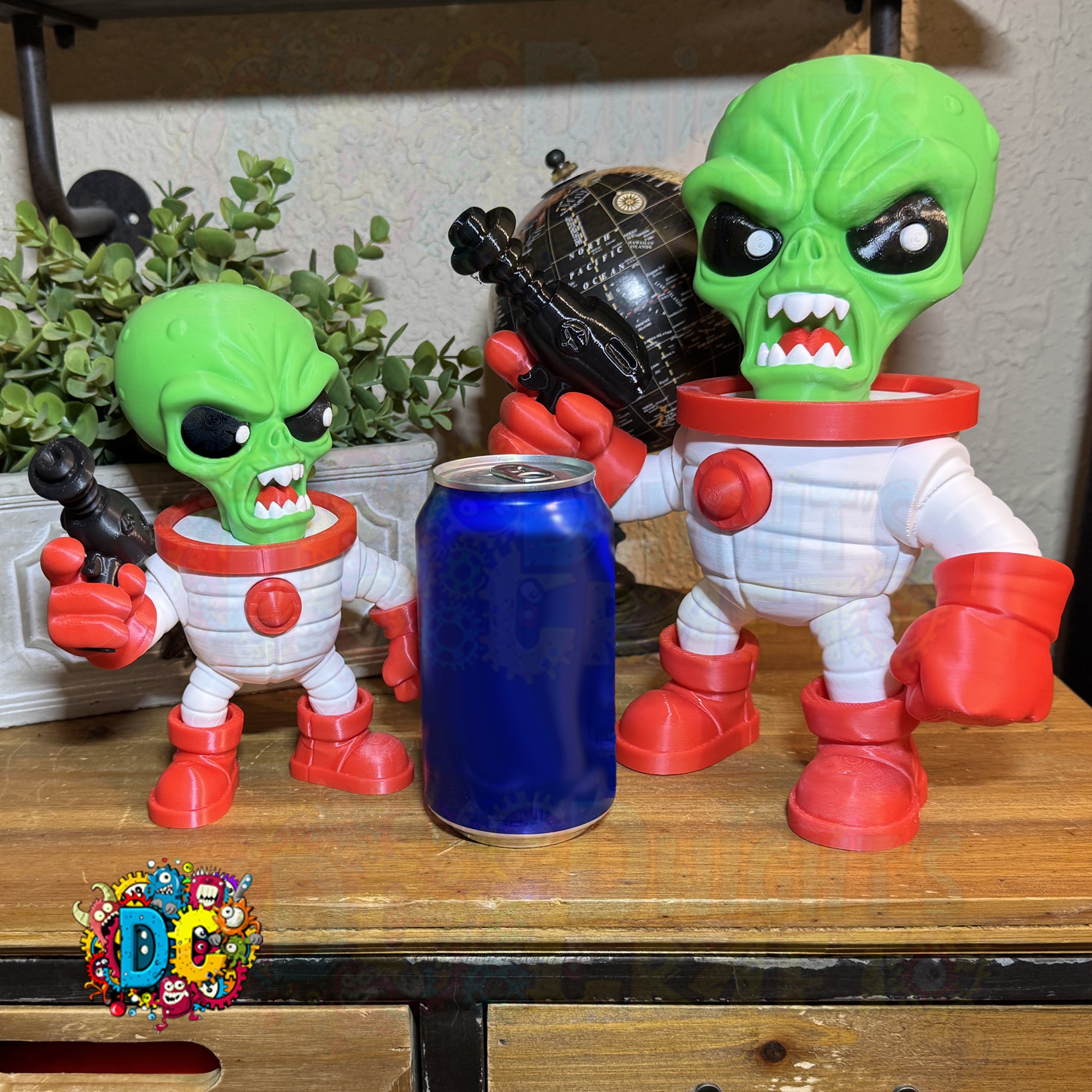 Two green alien figures with red boots holding a blue can on a wooden surface.