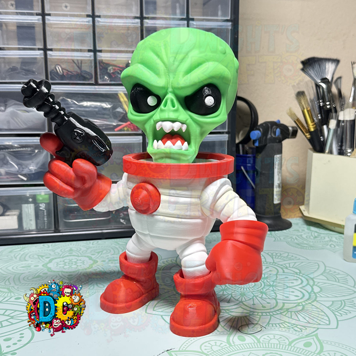 Toy figure of a green alien in a white suit with red boots on a table.