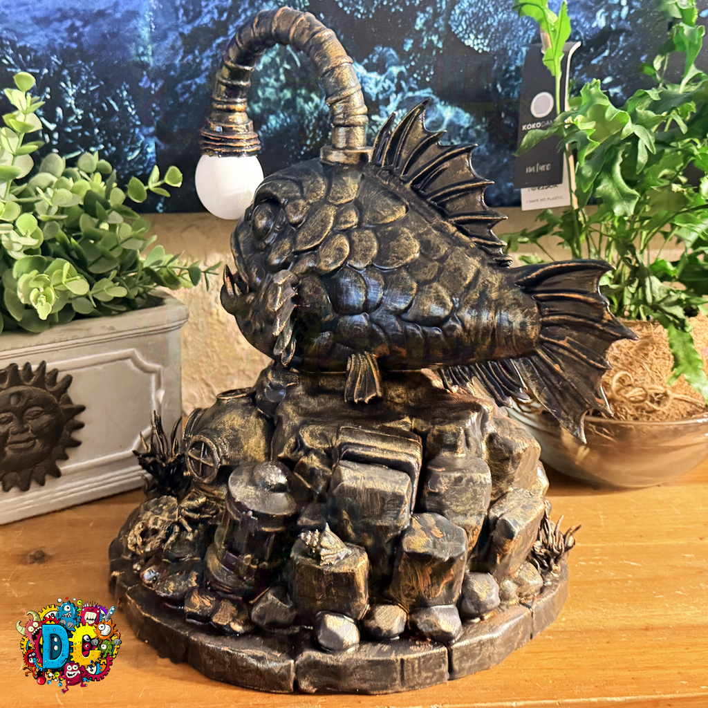 Decorative ambient lighting angler fish sculpture on a rocky base with plants in the background