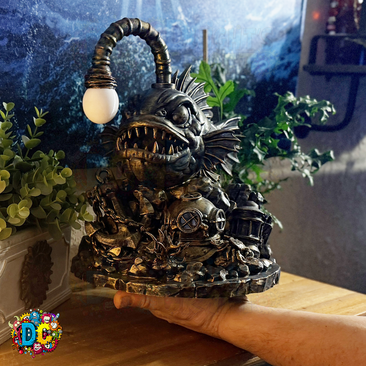 Decorative angler fish-shaped ambient light on its lure, held by a hand in a room with plants and a window.