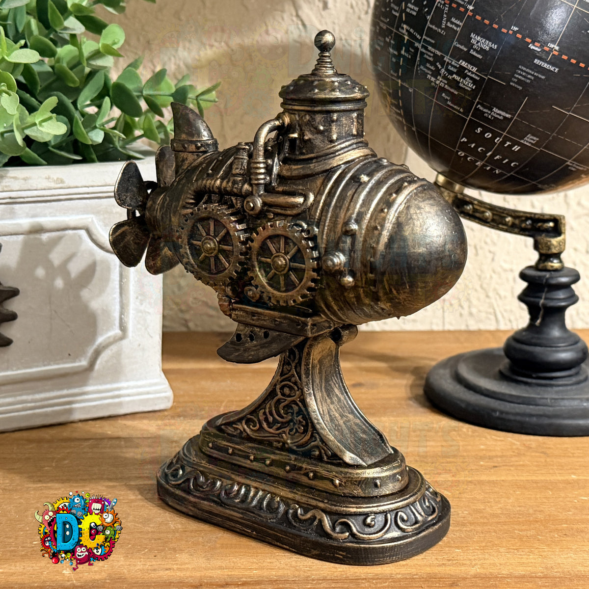 Decorative metal sculpture with gears on a wooden surface next to a potted plant and globe.