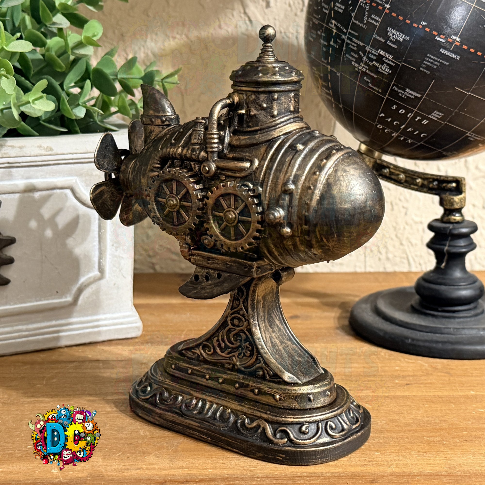 Decorative metal sculpture with gears on a wooden surface next to a potted plant and globe.