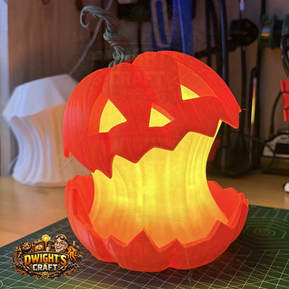 A 3D-printed jack-o'-lantern pumpkin light glowing from within, placed on a green cutting mat in a workshop setting. A 'Dwight's Craft' logo is visible in the bottom-left corner.