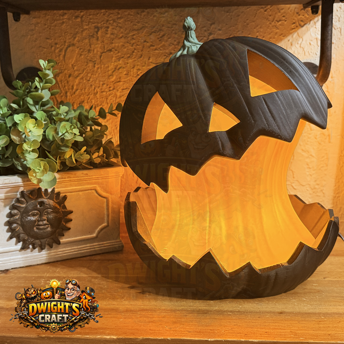 A carved jack-o'-lantern Halloween light with a dark textured exterior and glowing orange interior, displayed on a wooden shelf next to a potted plant. A 'Dwight's Craft' logo is visible in the bottom-left corner.