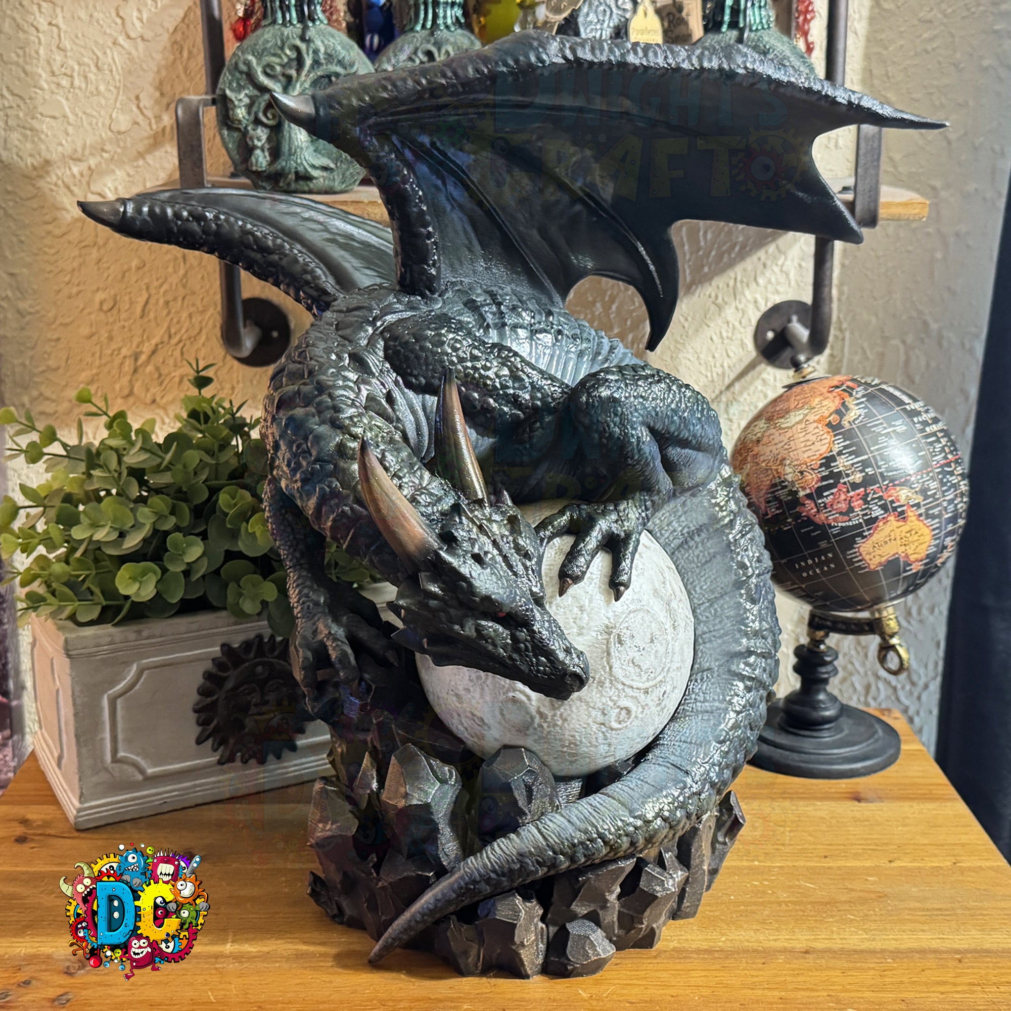 Decorative dragon sculpture holding a moon on a wooden surface with a globe and plants in the background.