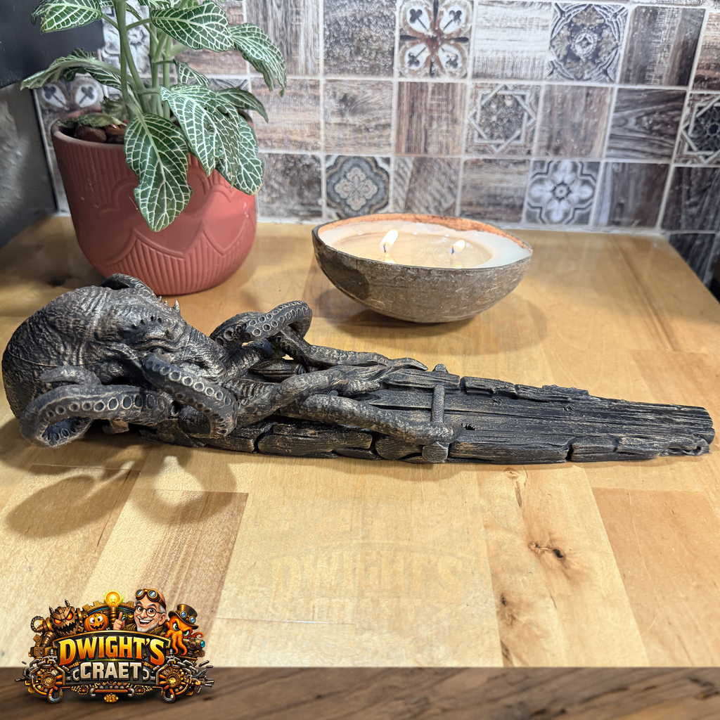 A dark, detailed octopus figurine resting on a weathered wooden plank, displayed on a light wood tabletop with a potted plant and a candle in the background. A 'Dwight's Crafts' logo is visible in the bottom-left corner.