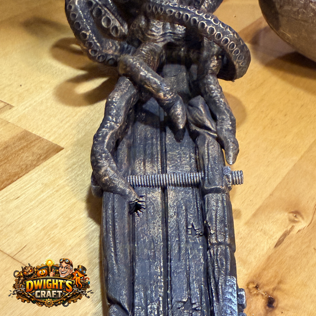 A close-up of a detailed miniature figurine depicting a creature with tentacles gripping a wooden plank, finished in a weathered dark gray and black paint with a distressed finish. The figurine is placed on a light-colored wooden surface, and a 'Dwight's Craft' logo is visible in the bottom-left corner.