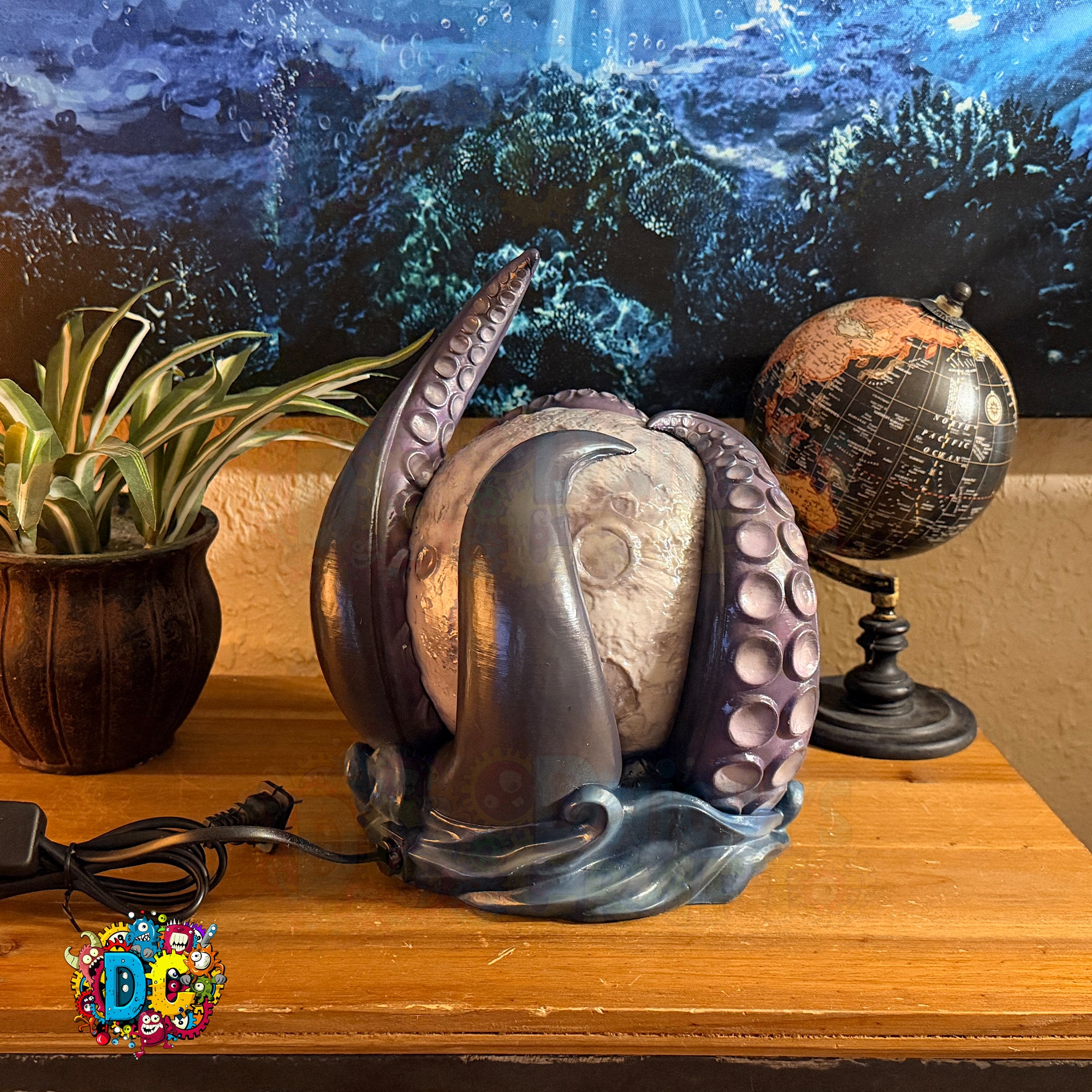 Decorative metal sculpture on a wooden surface with a globe and plant in the background