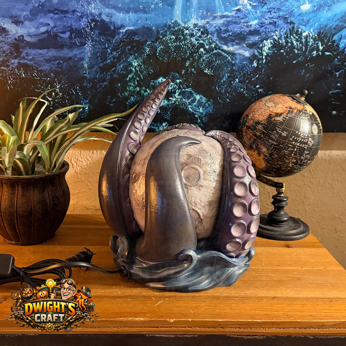 An octopus-themed night light by The Dwight's Craft, featuring a textured moon wrapped in purple tentacles on a blue wave base, displayed on a wooden shelf next to a plant and a globe.