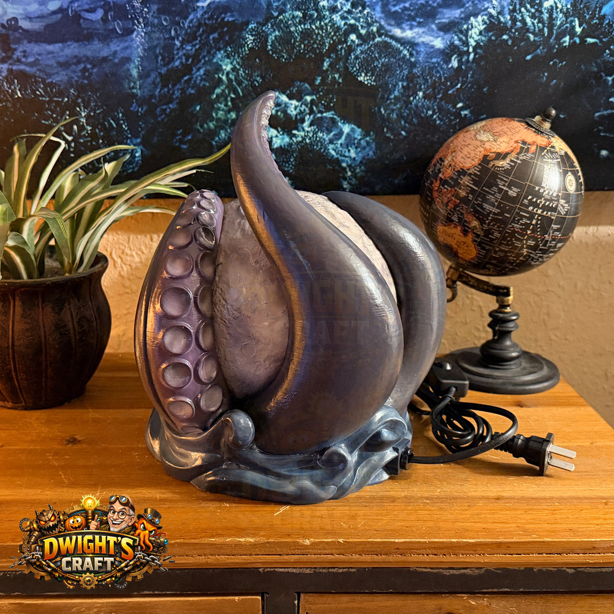 A fantasy-style octopus lamp with purple and blue-gray tentacles sits on a wooden table next to a globe and a potted plant. The lamp has a dark base with swirling blue-gray details and a visible power cord.