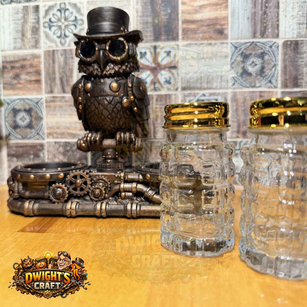 Two clear glass mason-jar style cups with gold lids in the foreground, alongside a steampunk owl figurine and decorative metal piece on a wooden surface, with a tiled wall behind. A 'Dwight's Craft' logo is visible in the lower-left corner.