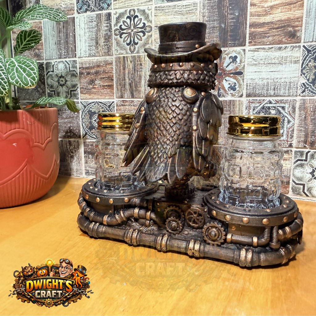 Steampunk-style decorative owl figurine in dark metallic bronze with a top hat, flanked by two clear glass jars with gold lids, displayed on a wooden surface against a patterned tile wall. A plant pot is visible on the left, and a 'Dwight's Craft' logo appears in the lower-left corner.