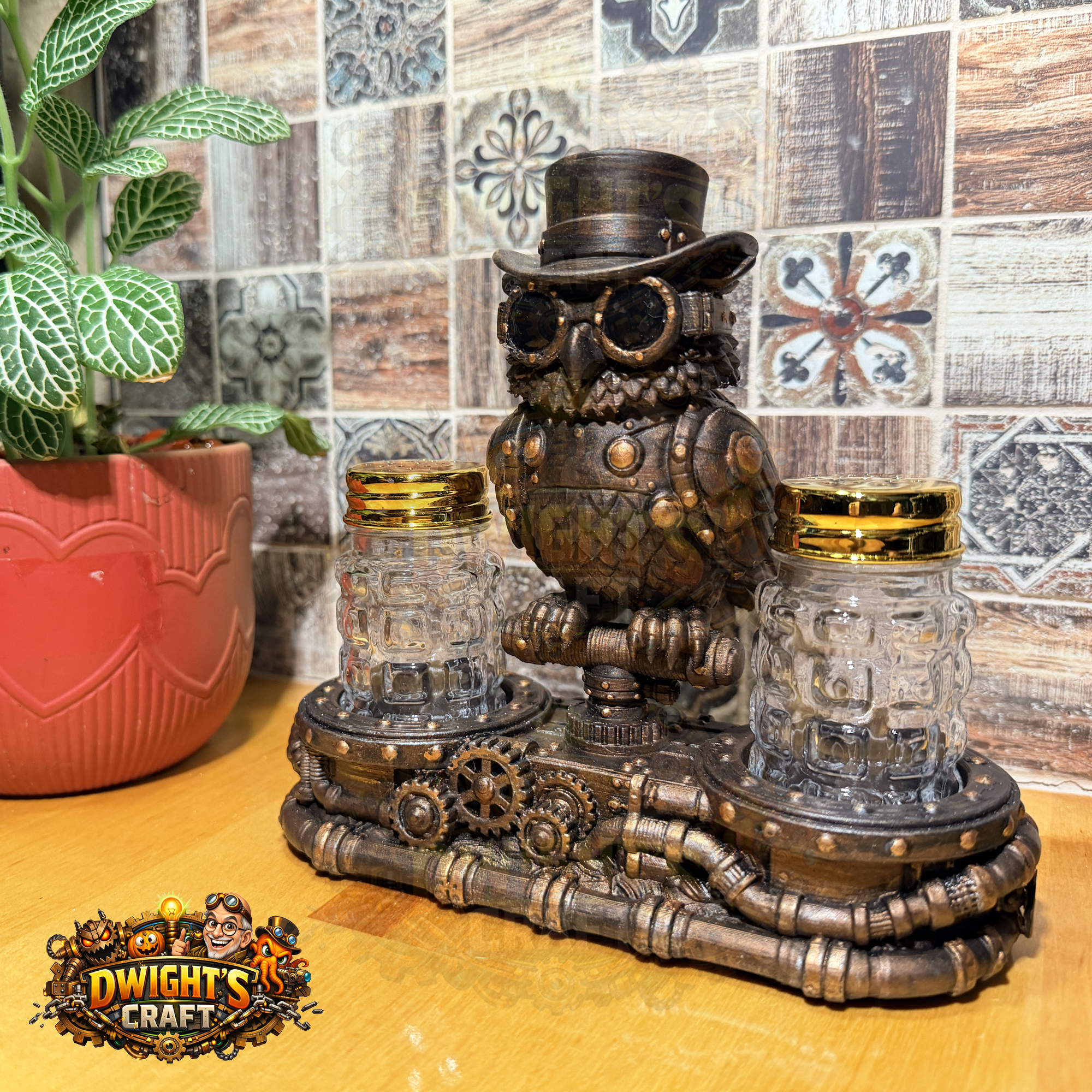 Steampunk owl candle holder with two glass mason jar candle holders on a decorative base, set on a wooden table with a tiled wall and a potted plant in the background. A 'Dwight's Craft' logo is visible in the bottom-left corner.